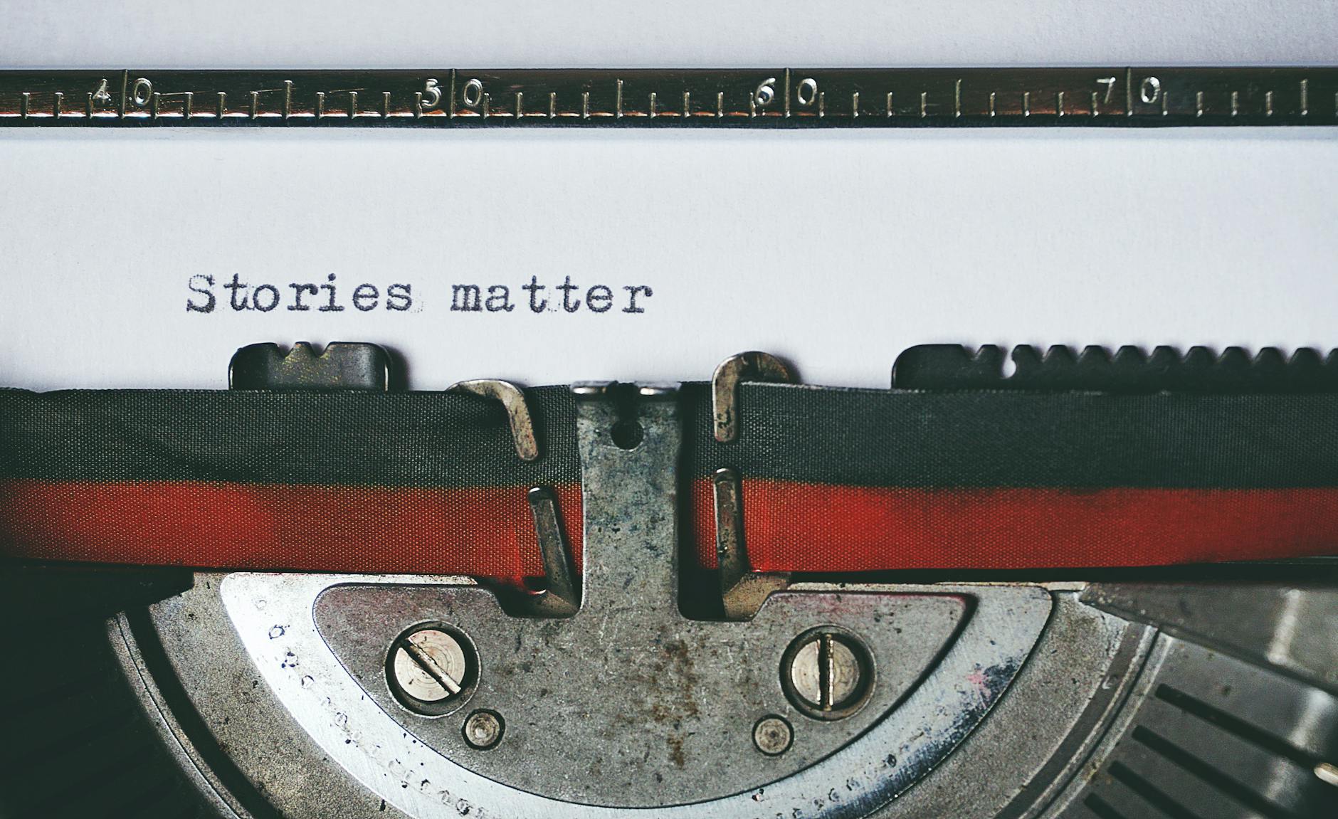 Close up on typewritten text on white paper in a typewriter. Text reads: "Stories matter"
